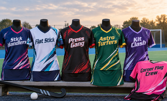 Six custom field hockey jerseys and skorts on a bench beside a turf pitch